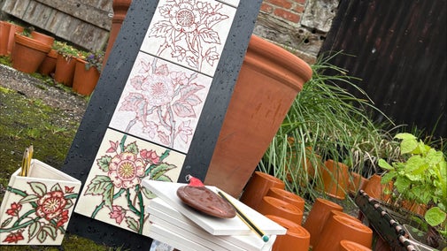 Ceramic tiles stacked in front of gradually painted tiles, flower pots and a barn